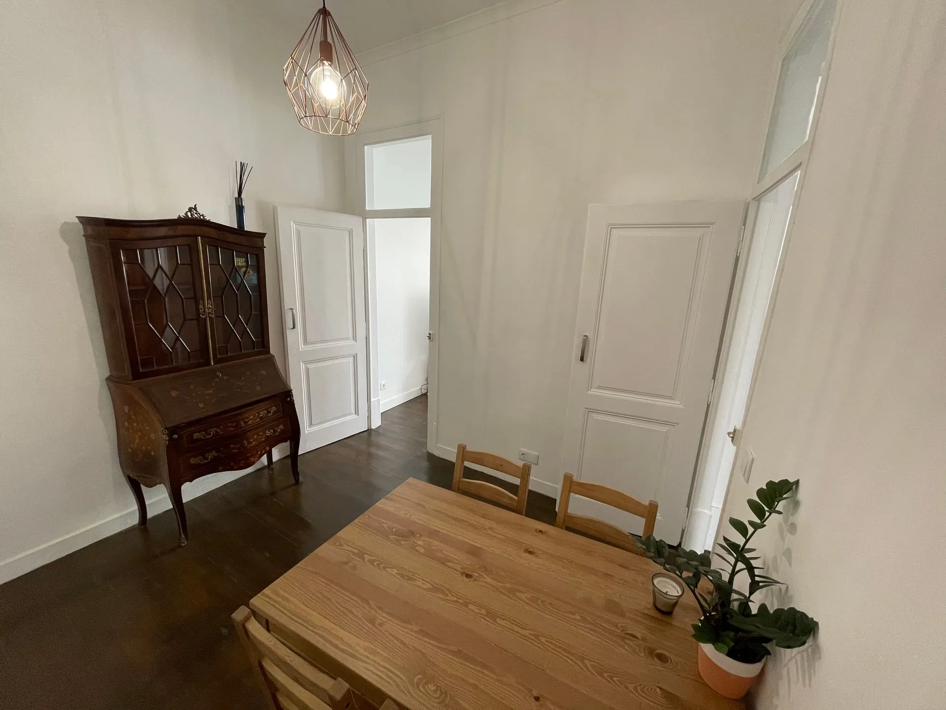 Jadalnia w lizbońskim apartamencie — drewniany stół, antyczny sekretarzyk i geometryczna lampa