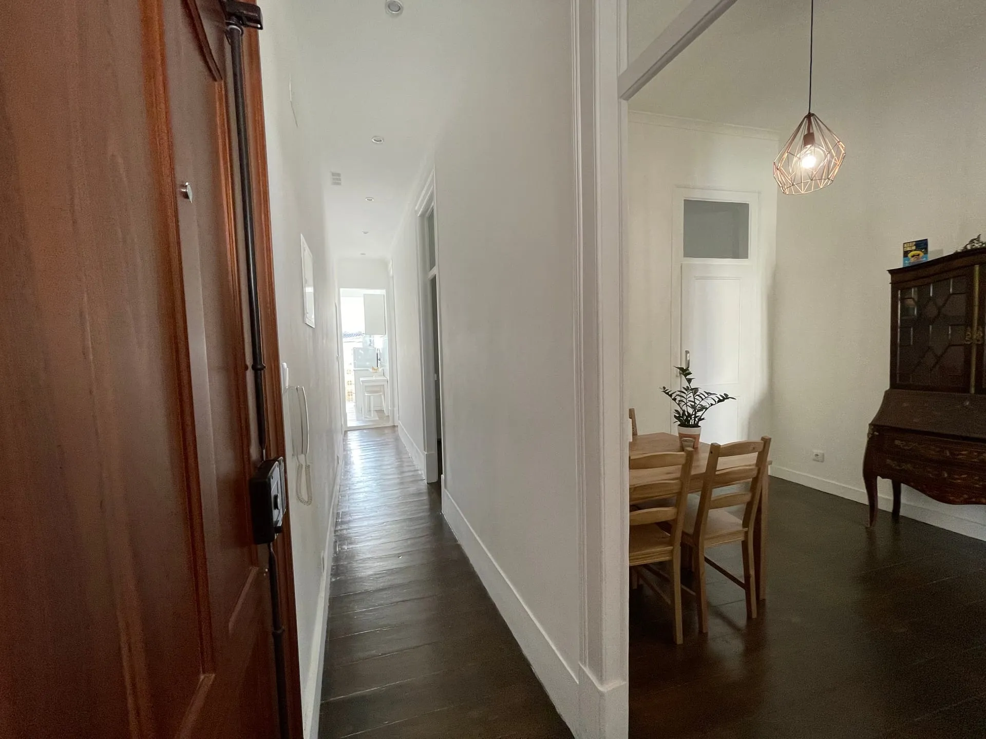 Korytarz odnowionego apartamentu w Lizbonie — ciemne drewniane podłogi i geometryczna lampa