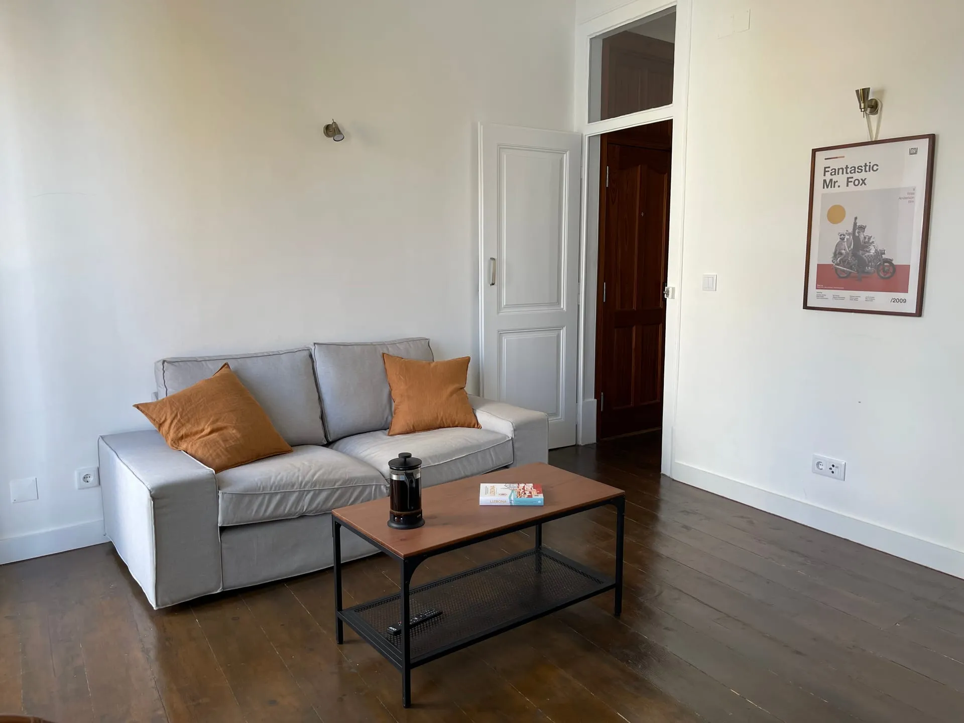 Salon apartamentu z szarą sofą i terakotowymi poduszkami — ciemne drewniane podłogi