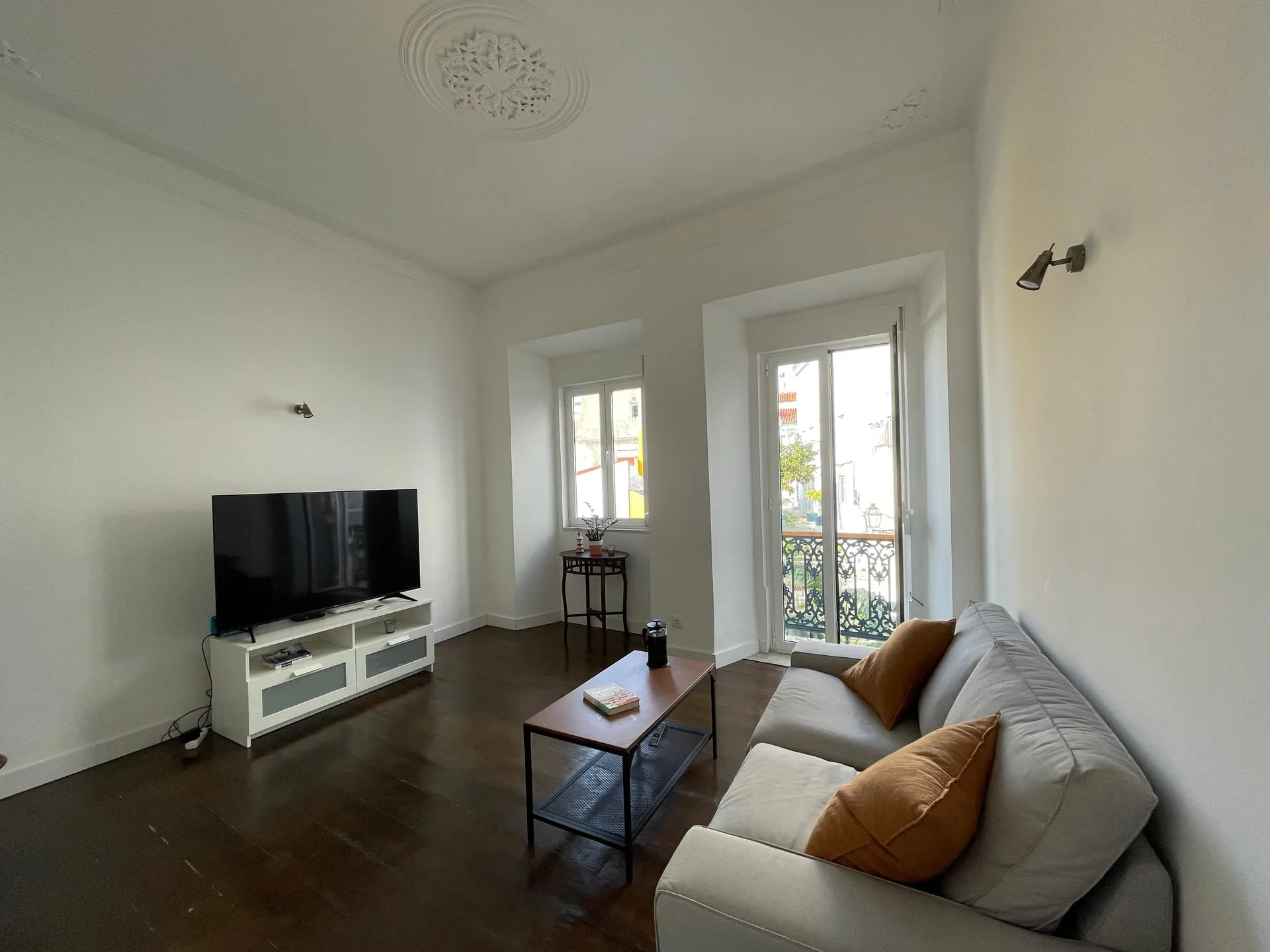 Salon z wysokimi oknami i balkonem francuskim w wyremontowanym lizbońskim apartamencie