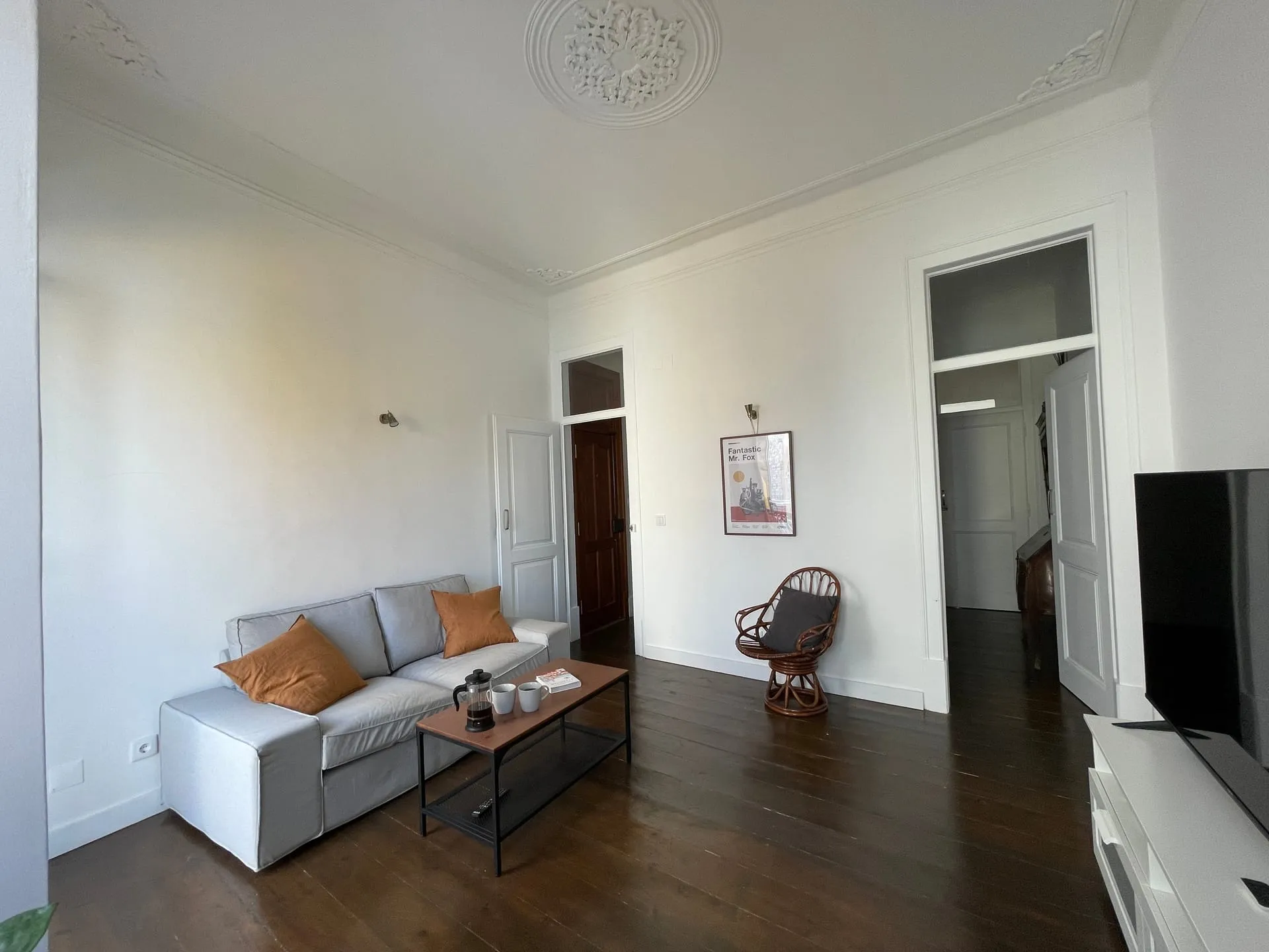 Salon lizbońskiego apartamentu z rattanowym fotelem i szarą sofą