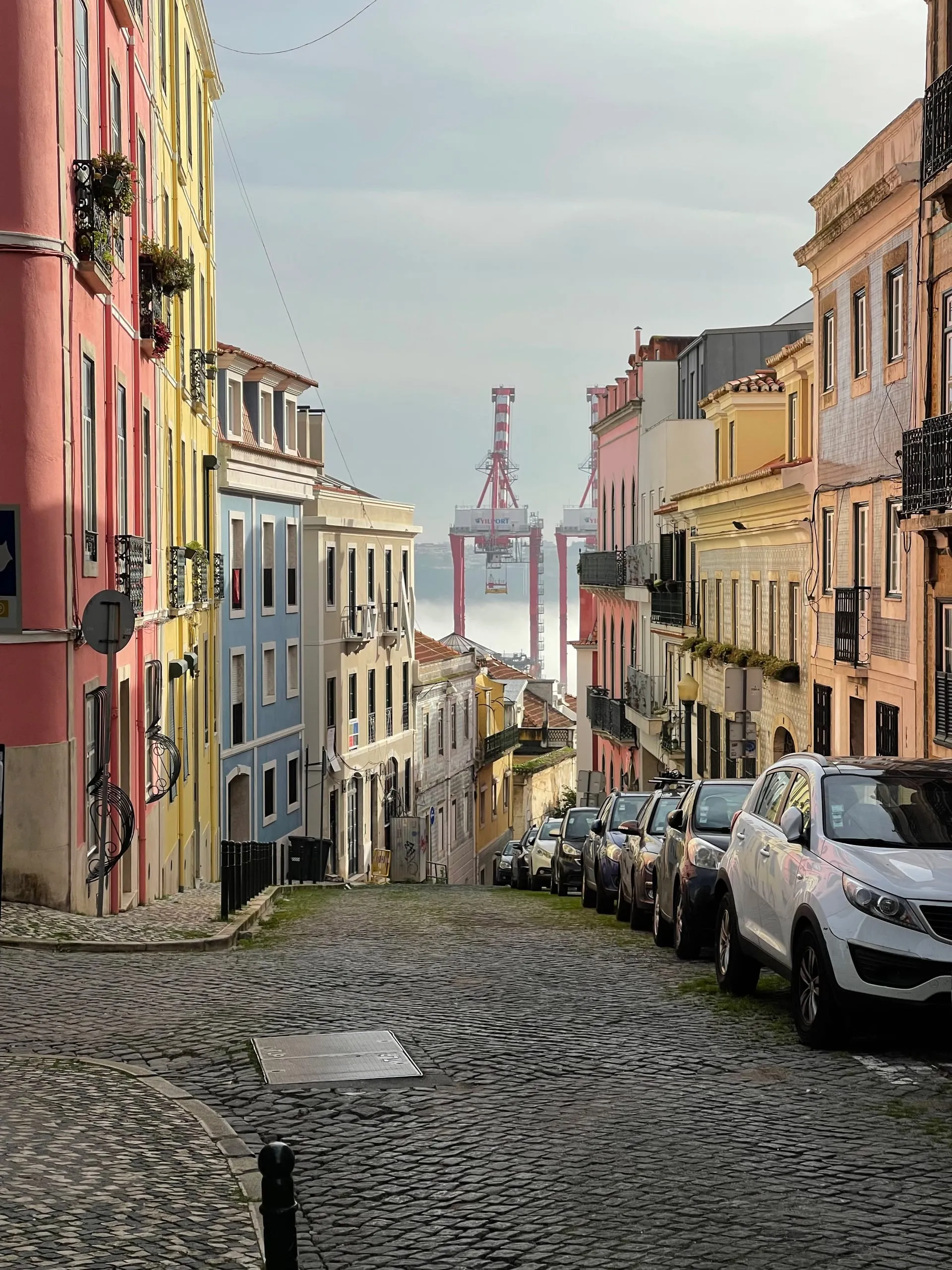 Kolorowe kamienice na lizbońskiej uliczce z brukowaną nawierzchnią — Ponte 25 de Abril w tle